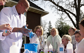 Mad scientist with hands in the air and microphone holding a beaker with a red liquid and smoke pouring out